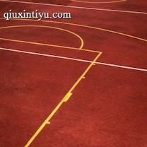 A sports court with a reddish-brown surface and bright yellow and white lines. The lines form geometric shapes, including rectangles and circles, suggesting markings for games like basketball or netball.